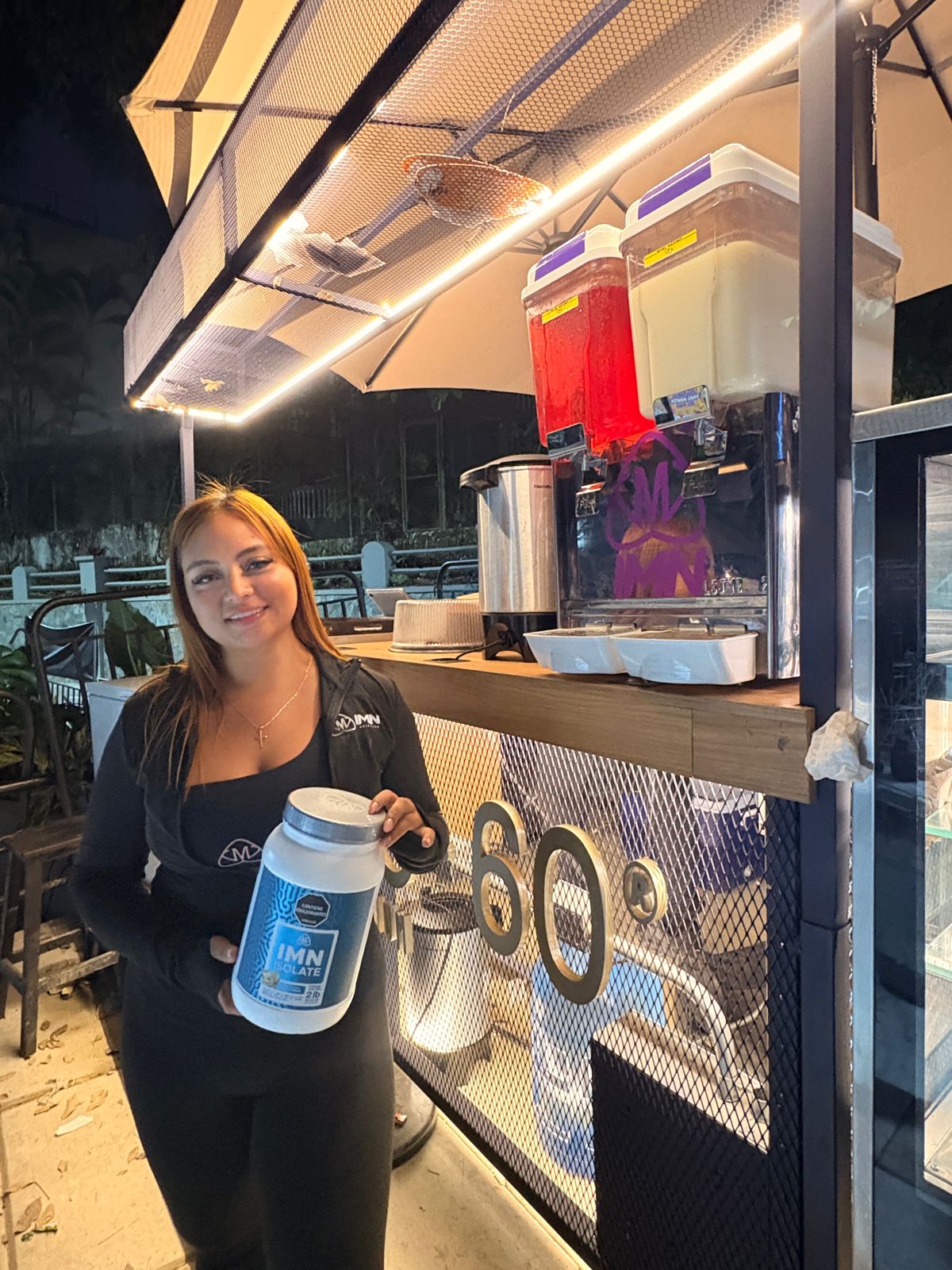 Promotora IMN con un IMN Isolate de 2 lb junto a una granizadora doble con el logo de IMN