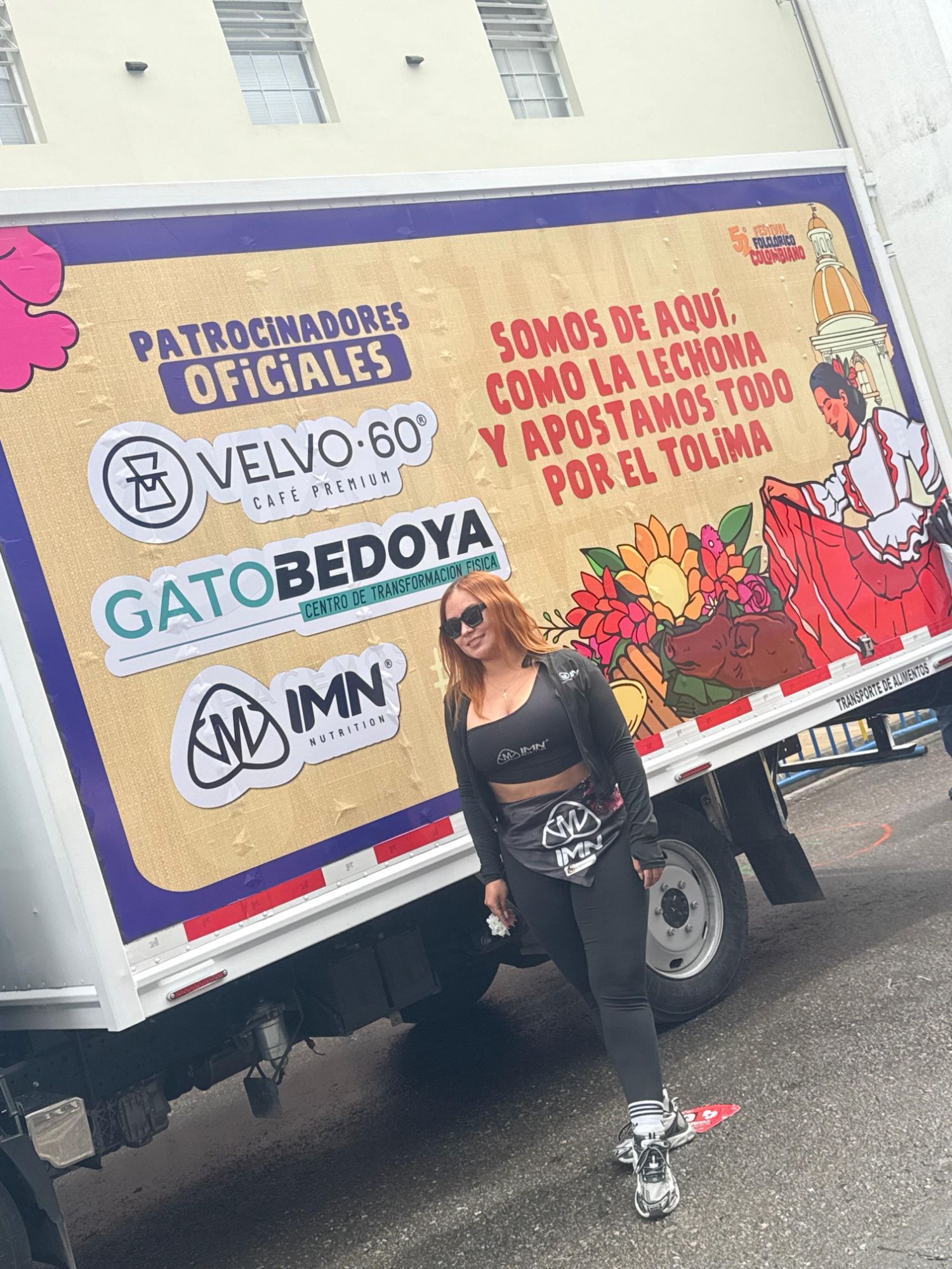 Promotora IMN con uniforme de la marca frente a un camión de patrocinadores oficiales del Festival Folclórico Colombiano donde aparece el logo de IMN Nutrition
