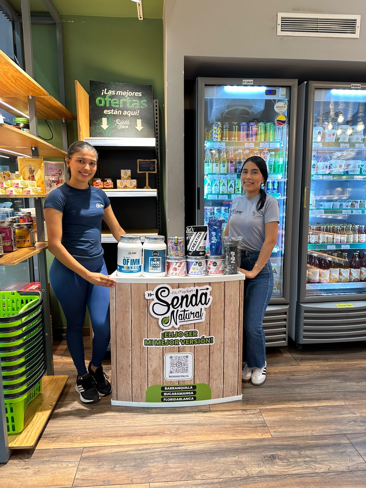 Dos promotoras IMN junto al exhibidor de producto IMN dentro de una tienda saludable